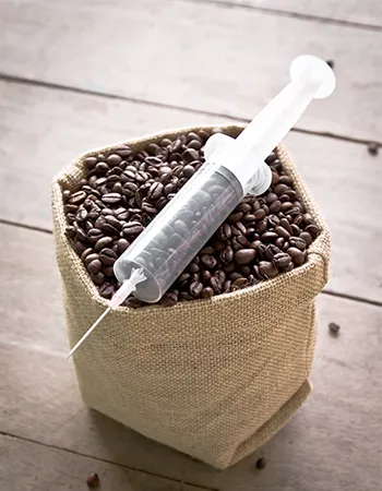 Syringe in a coffee cup representing coffee enema therapy — a holistic detox method that supports liver function, bile flow, and toxin elimination.