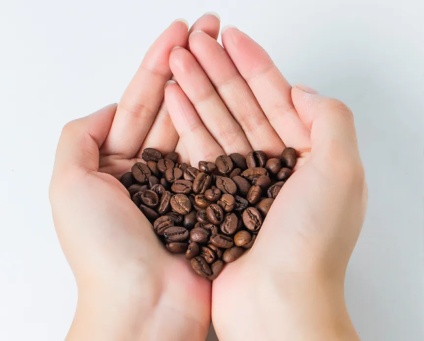 Heart-shaped coffee beans held in hand, representing the natural detox benefits of coffee enemas that enhance bile production and support liver function.