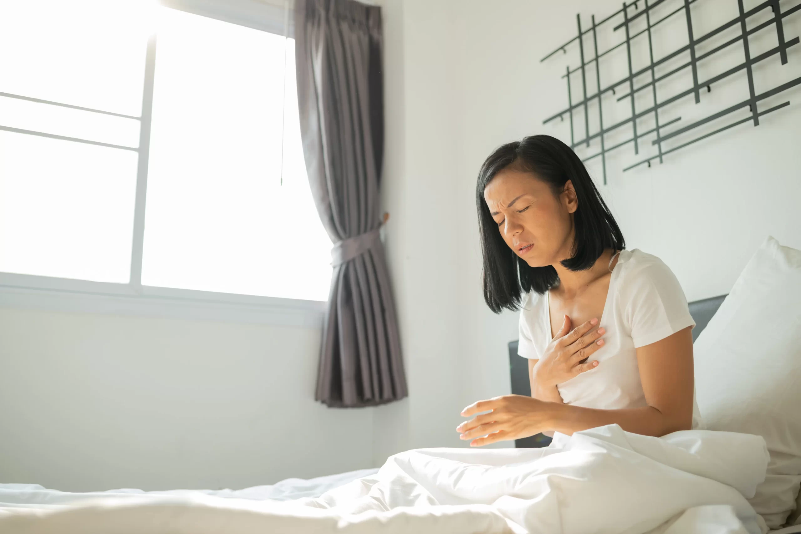 Asian woman experiencing chest pain and fatigue in bed — illustrating early warning signs of a heart attack in women, often mistaken for general tiredness or stress.