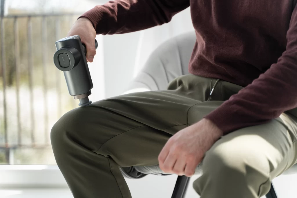 Man using massage gun for muscle stimulation — representing non-invasive approaches like Shockwave Therapy for Erectile Dysfunction (SWTD) that enhance circulation and treat the root causes of erectile dysfunction.